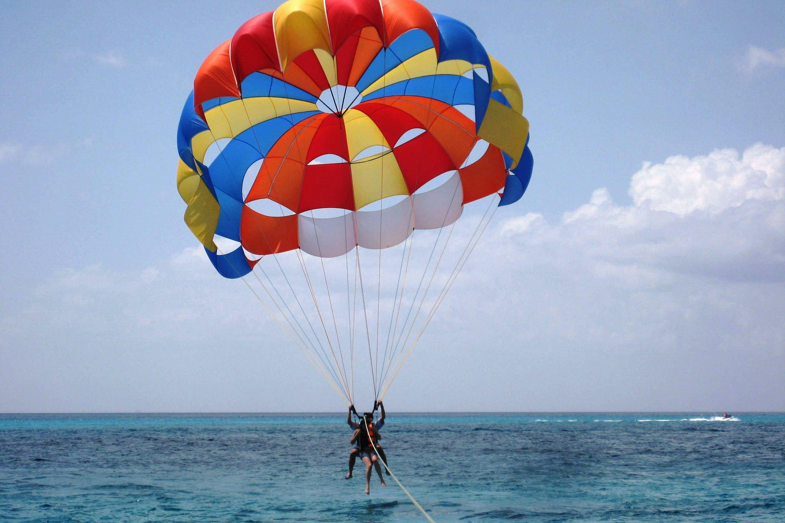 Two people parasailing over the ocean with a colorful parachute against a clear, blue sky.