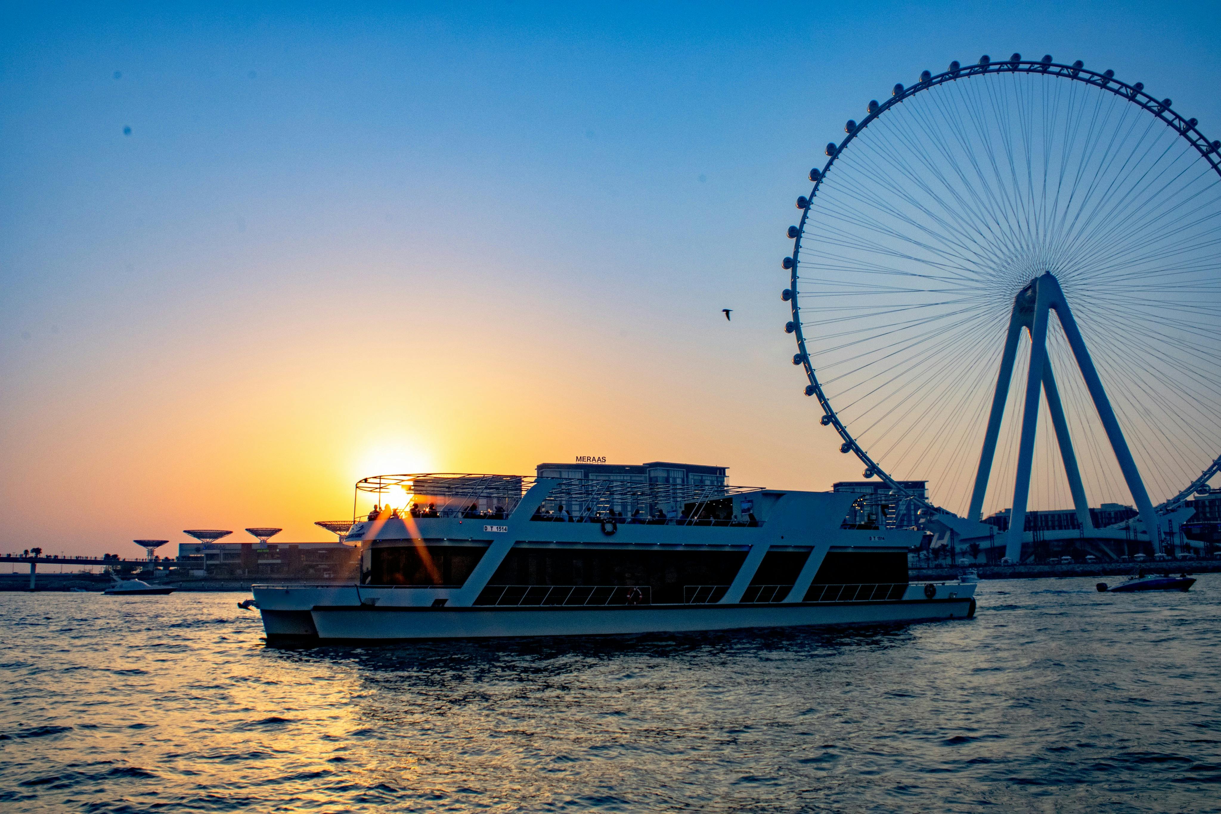 Loď na vodě při západu slunce s velkým ruským kolem v pozadí. Poblíž létá pták.