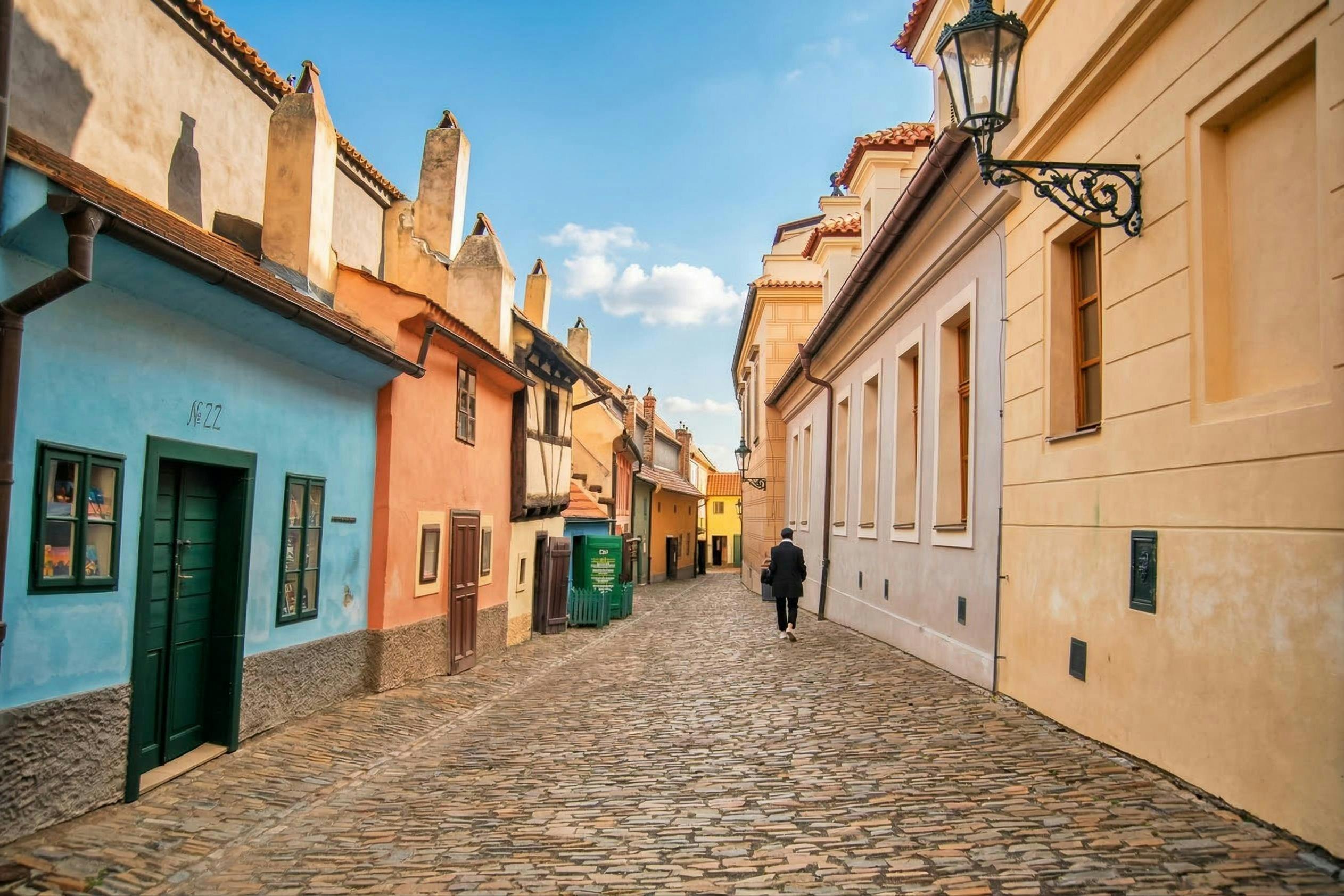 A narrow cobblestone street lined with colorful buildings, with a single person walking away under a clear blue sky.