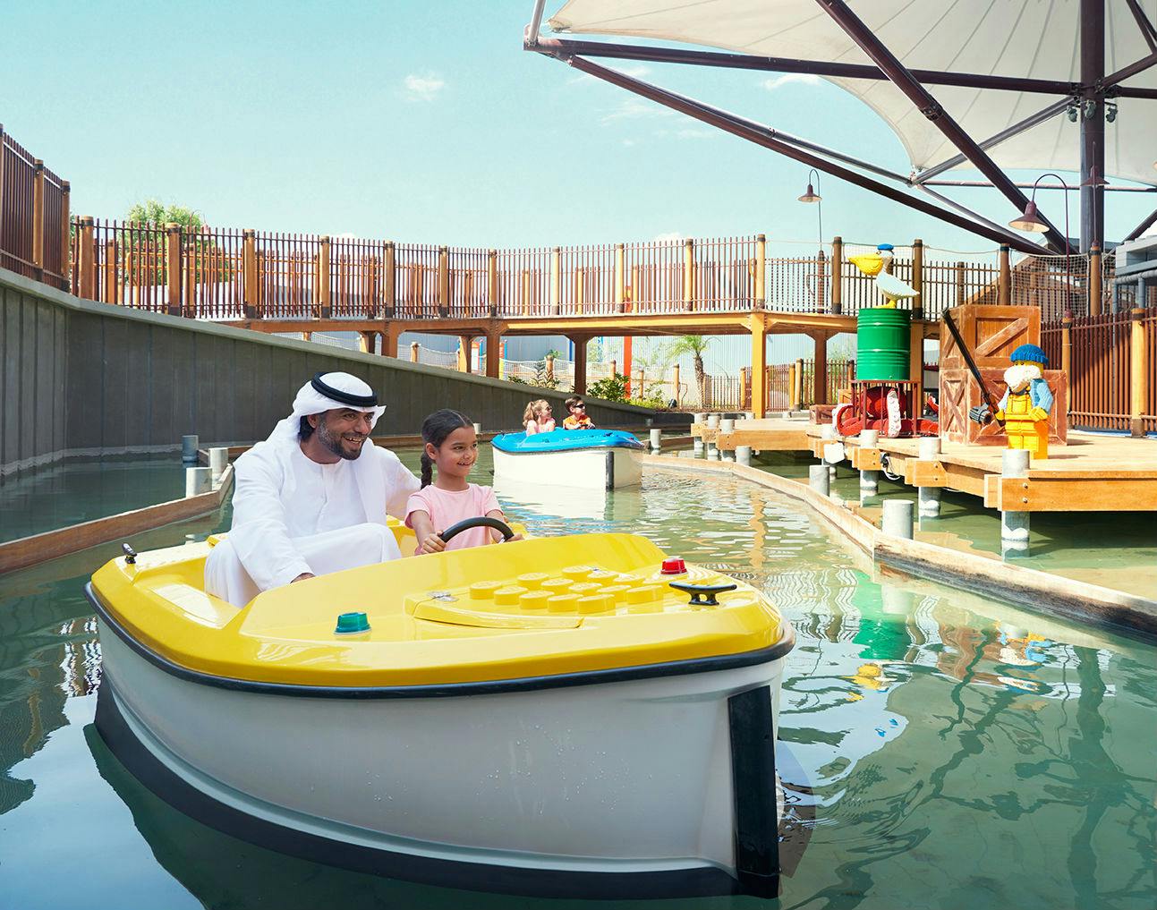 一个男人和一个女孩在水上乐园里驾驶一艘黄色踏板船。 背景中有其他人坐船。