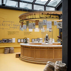 Ett kafé med en träbänk, stora fönster, burlap kaffesäckar och inredning med vintage kafferelaterade skärmar.