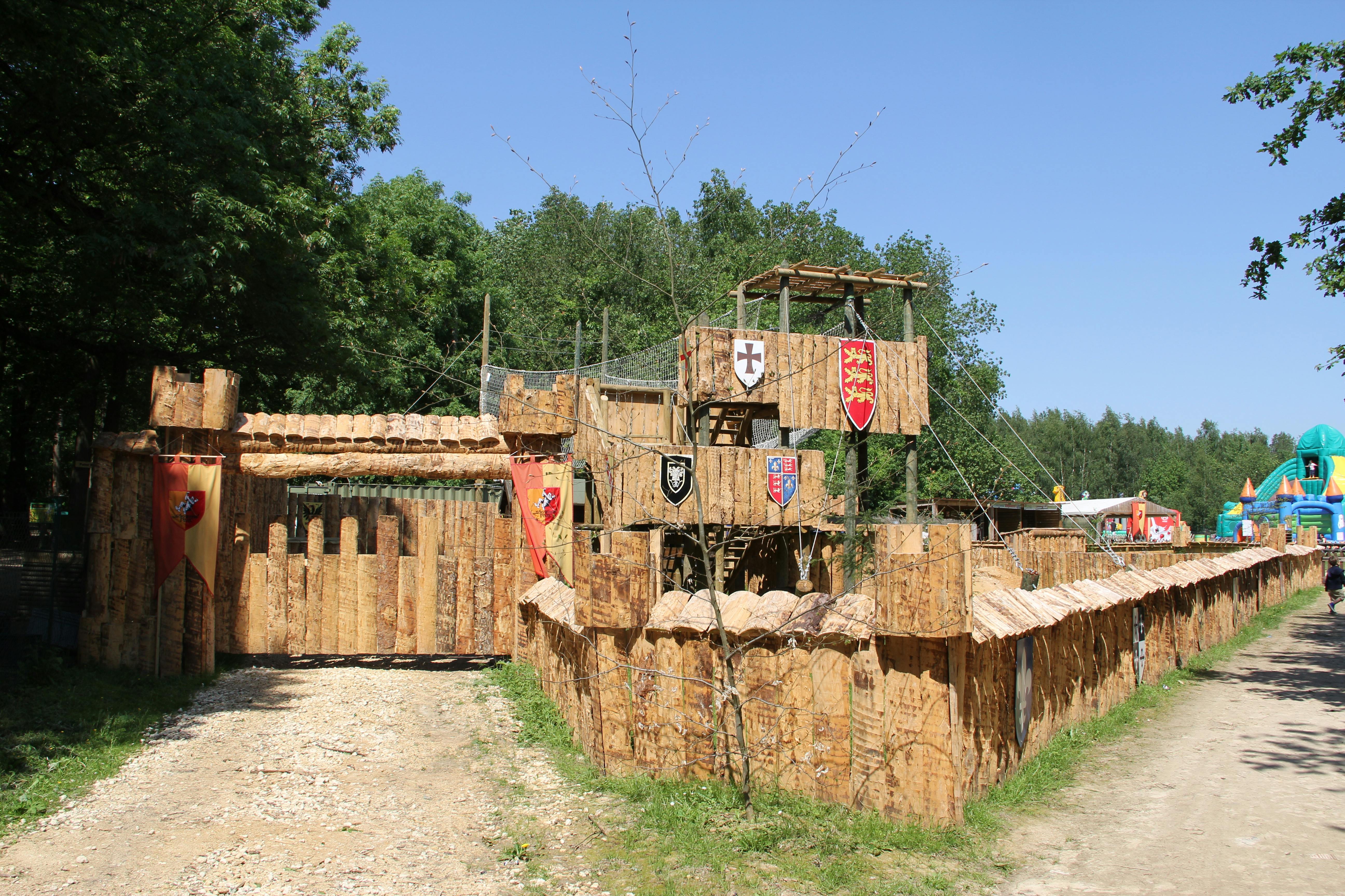 맑고 푸른 하늘 아래 숲이 우거진 곳에 타워, 산책로, 깃발 현수막이 있는 목조 성곽 구조물.