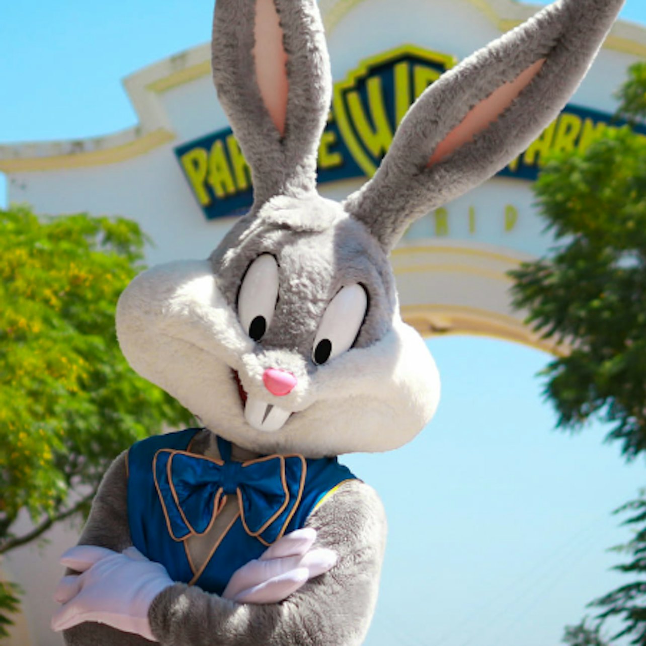 Person i en Bugs Bunny-dräkt som står med armarna i kors framför Warner Bros.-logotypen och ingången, med träd i bakgrunden.