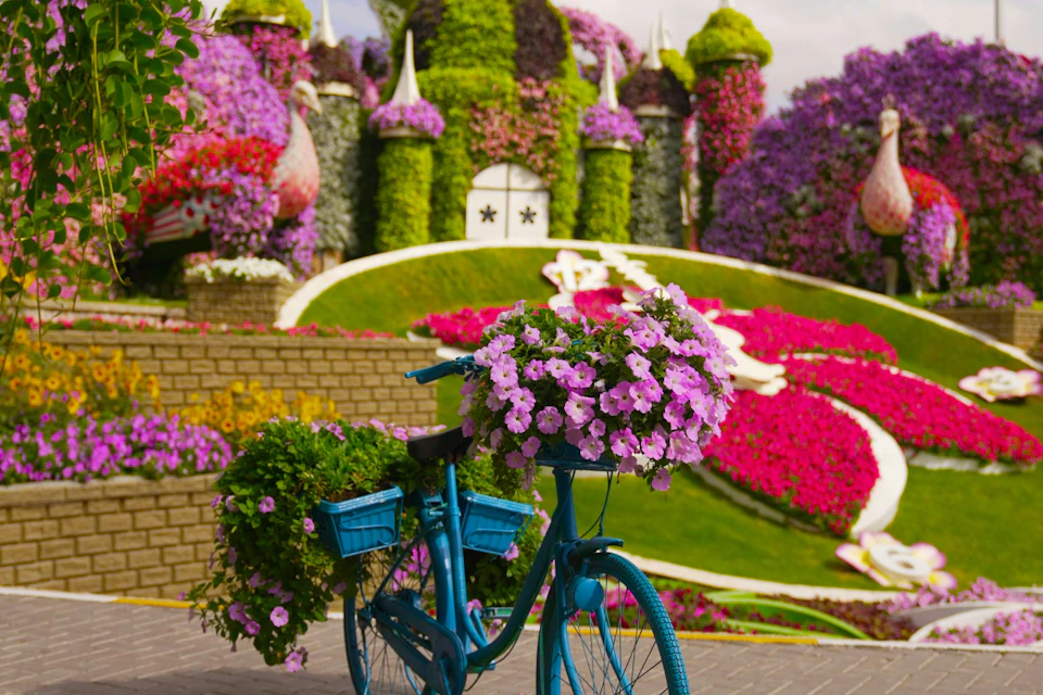 A blue bicycle with baskets of flowers in front of a garden castle adorned with vibrant floral arrangements.