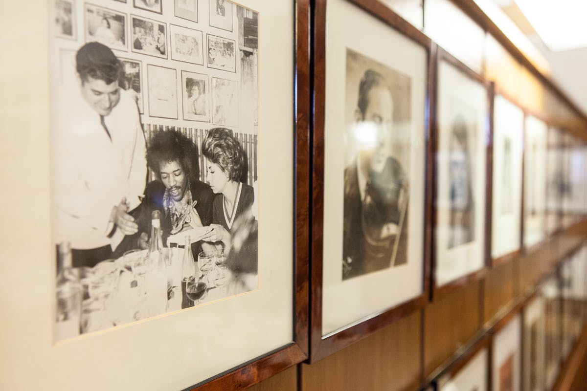 В рамке черно-белая фотография трех человек в ресторане, на которой один мужчина подает еду, а другие сидят за столом.