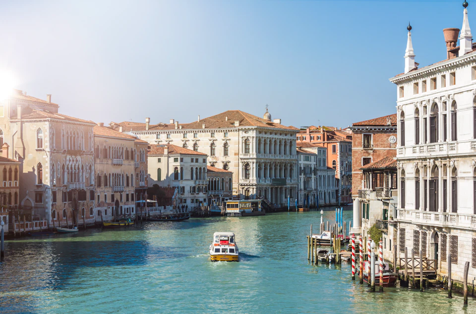A boat navigates a canal surrounded by historic buildings with a clear blue sky above.