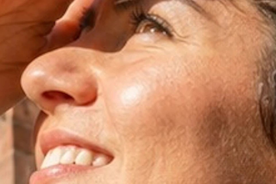 A woman shielding her eyes with her hand, looking up at ornate Gothic cathedral architecture under a clear blue sky.