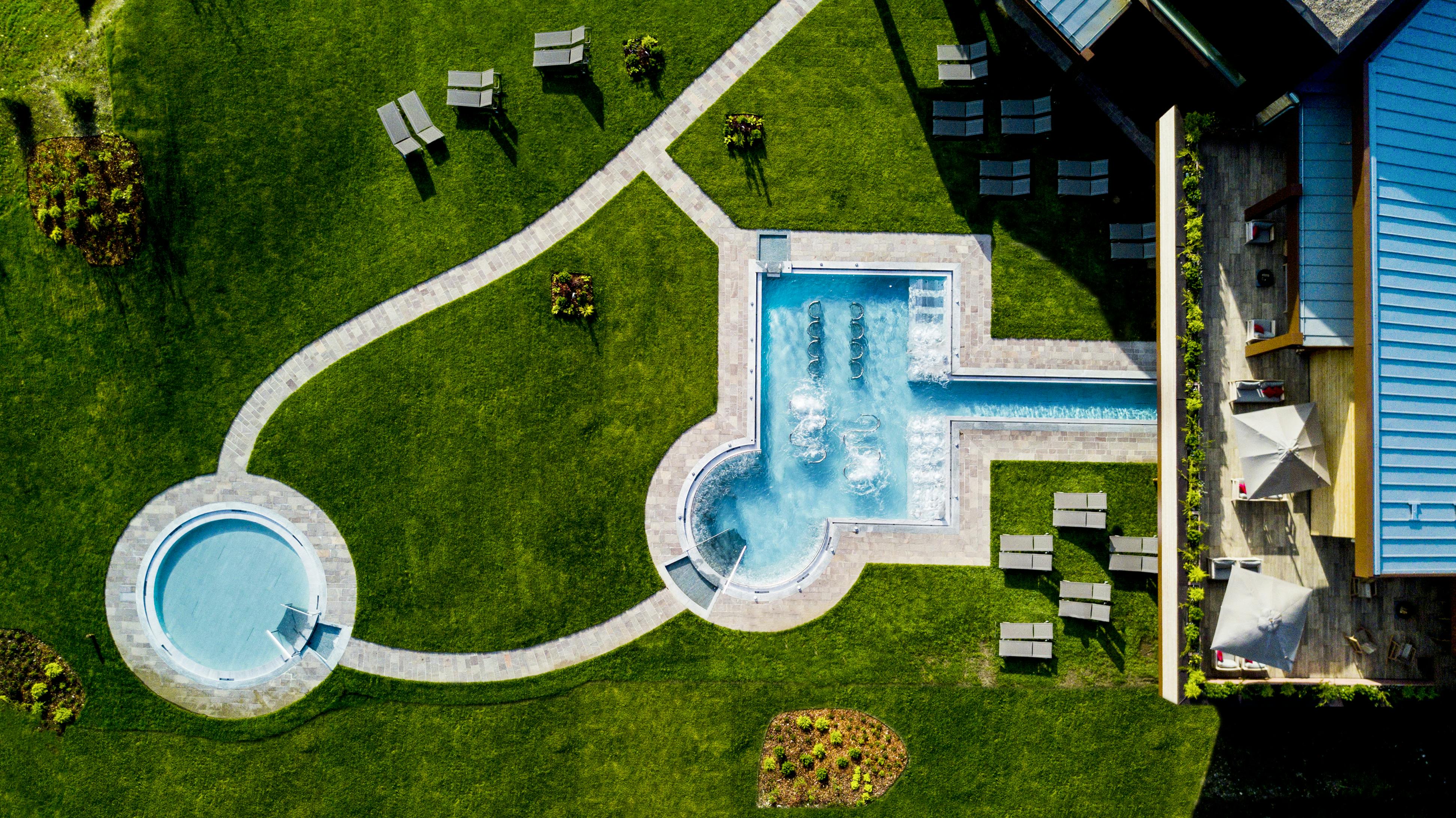 鸟瞰景观区域，带有长方形泳池，周围环绕着绿色的草地、小径和几张躺椅。