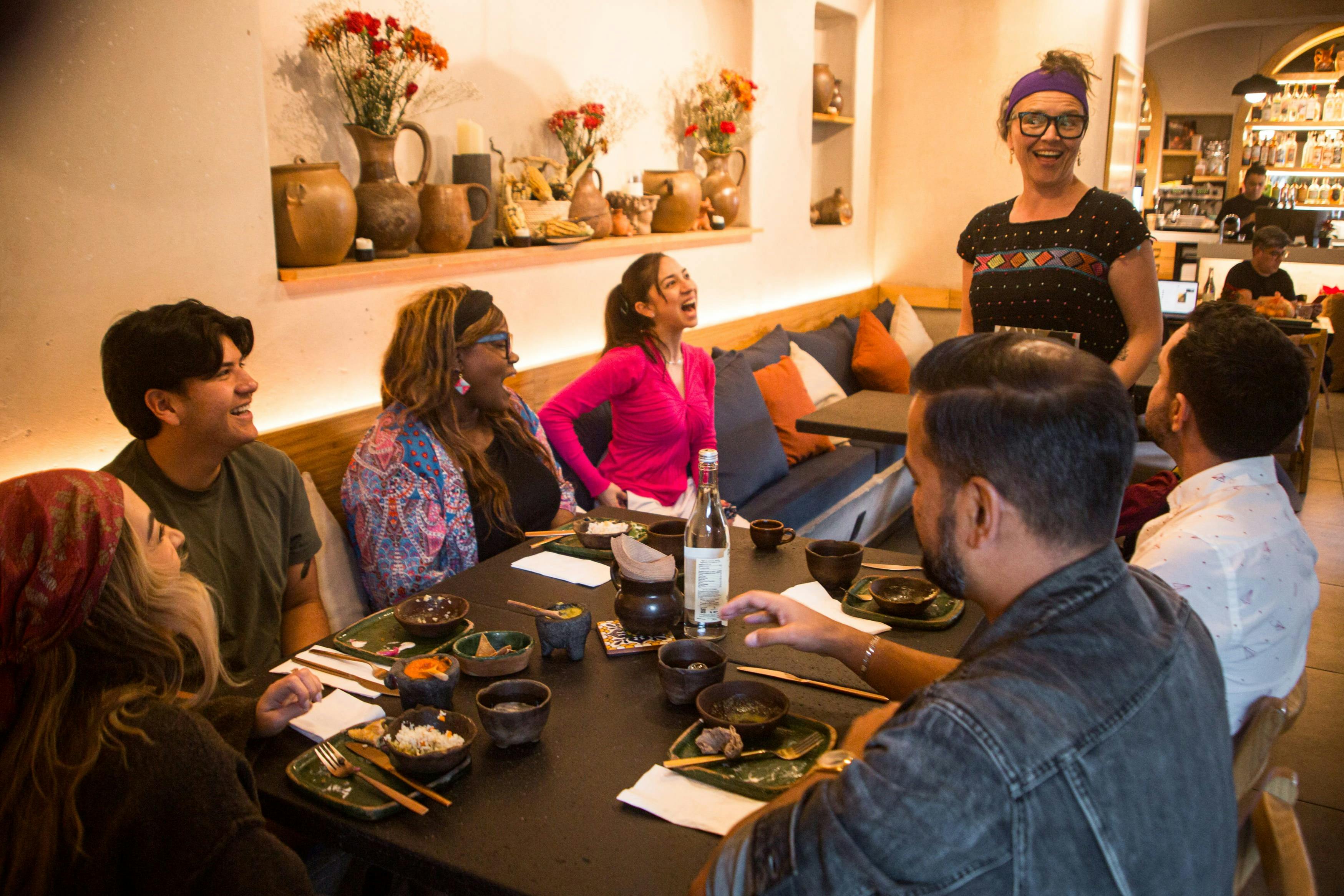 Un gruppo di persone è seduto intorno a un tavolo in un ristorante accogliente, ridendo e godendosi un pasto insieme.