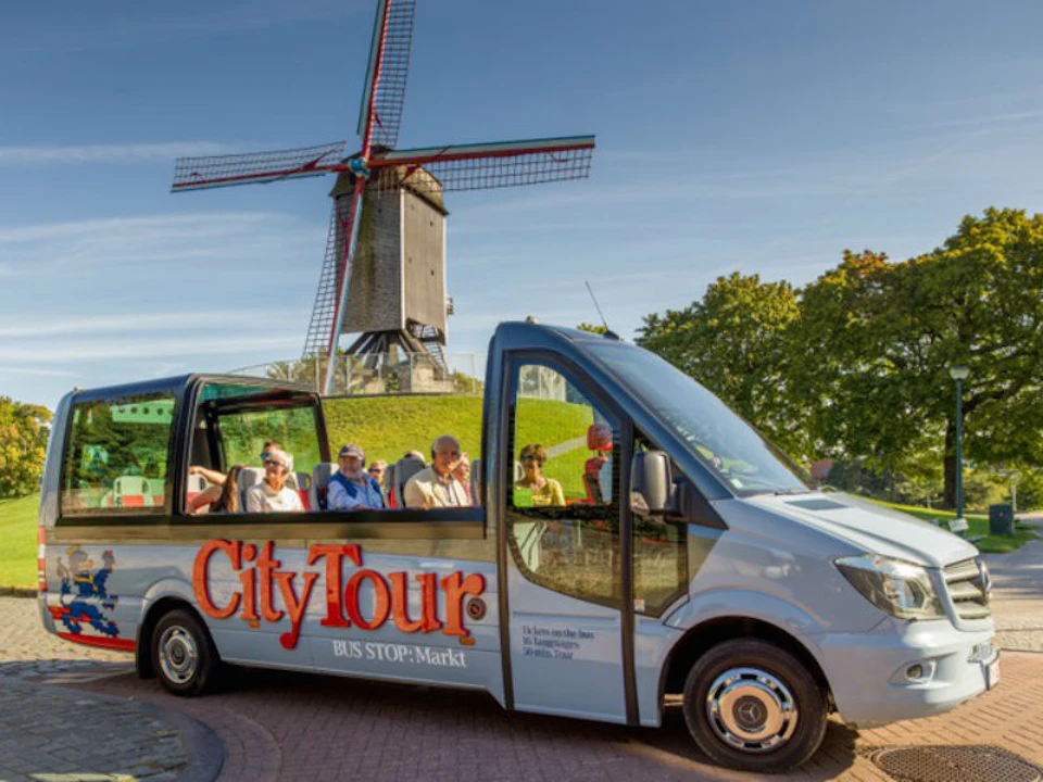 A tour bus with "CityTour" branding parked near a windmill, with passengers seated and greenery in the background.