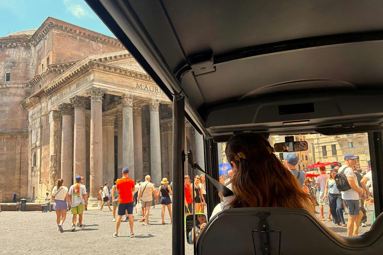 Interior view from the back of a vehicle with a person seated, looking out at a busy street with historical architecture.