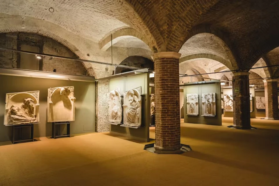 Underground museum gallery with brick arches, showcasing classical stone sculptures on green walls.