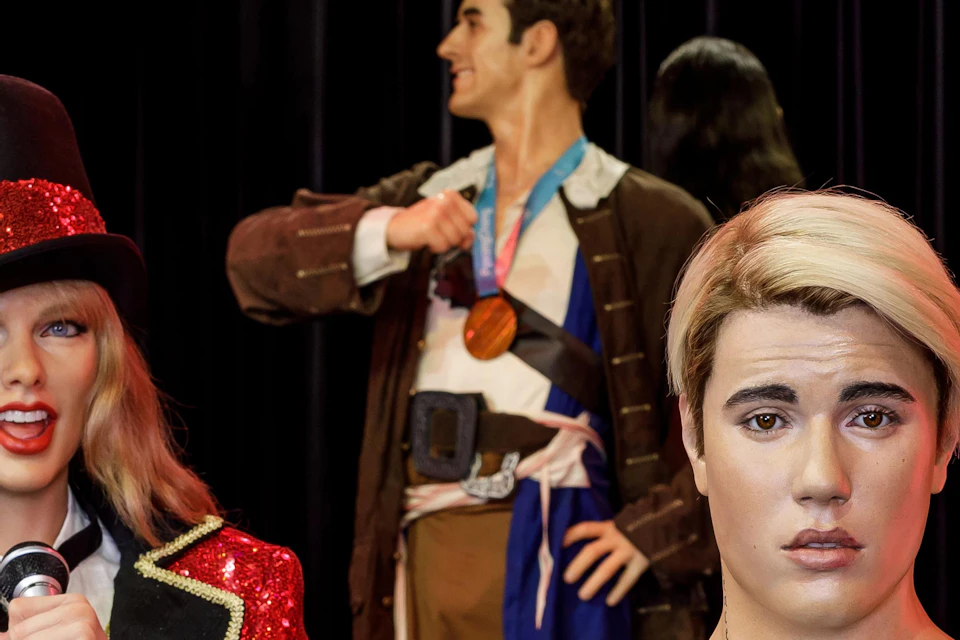 Figures in a wax museum: a man with tattoos, a woman in a sparkly red jacket, and another woman in pink pants holding a drink.