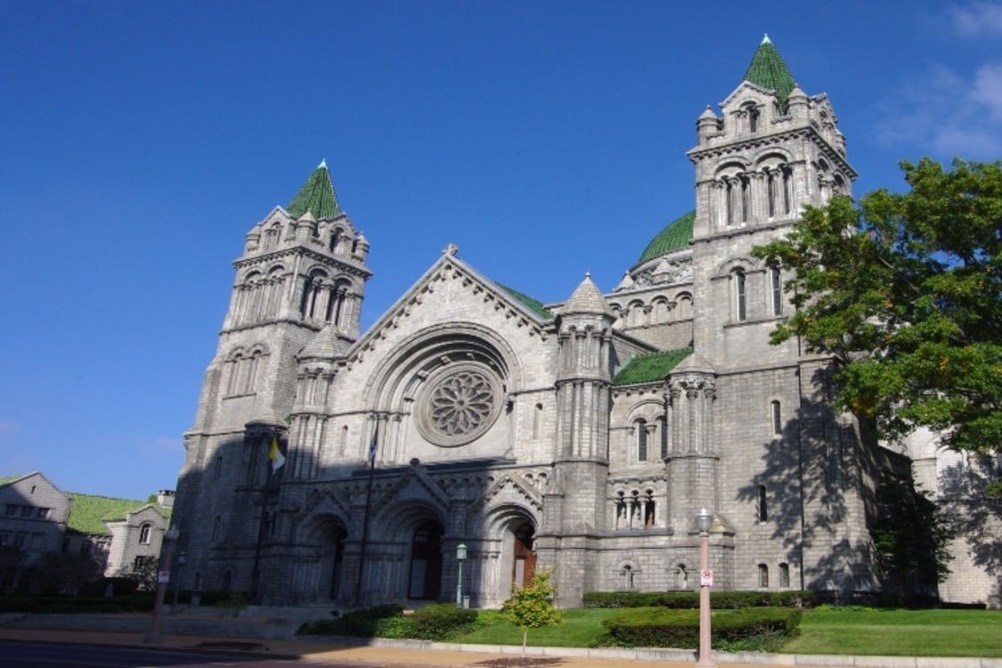 Ένας μεγάλος, περίτεχνος πέτρινος καθεδρικός ναός με πράσινες κεραμοσκεπές, μεγάλο στρογγυλό παράθυρο και δύο πύργους κάτω από έναν καταγάλανο ουρανό.