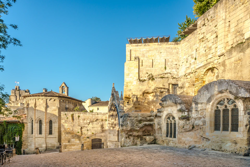 Historic stone buildings and structures under a clear blue sky, with arched windows and a cobbled courtyard.