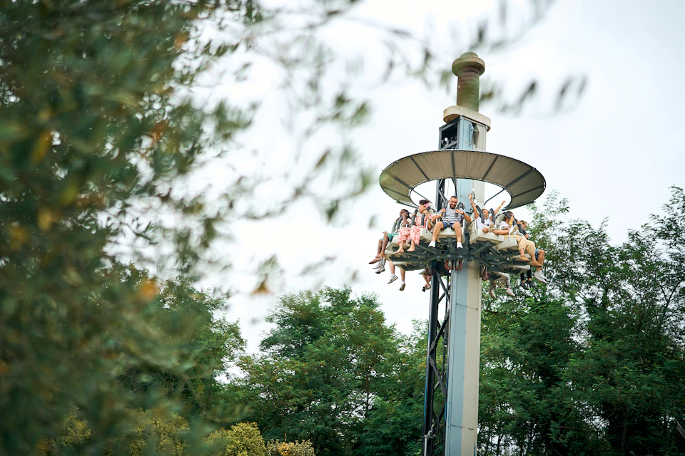 People sitting on an elevated amusement park ride surrounded by greenery.