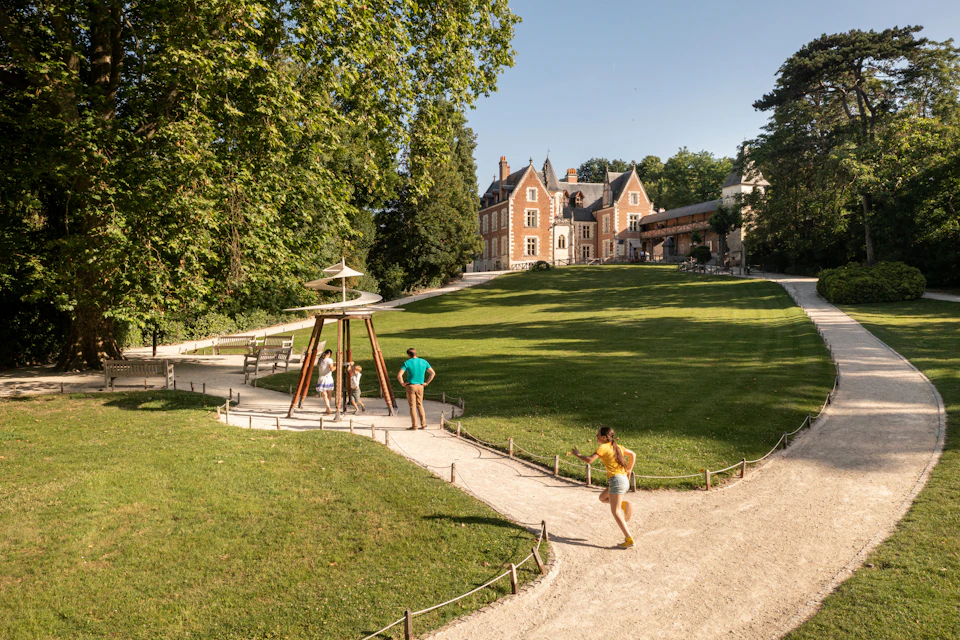A green lawn with a paved path, a play structure, people, and a large brick building in the background.
