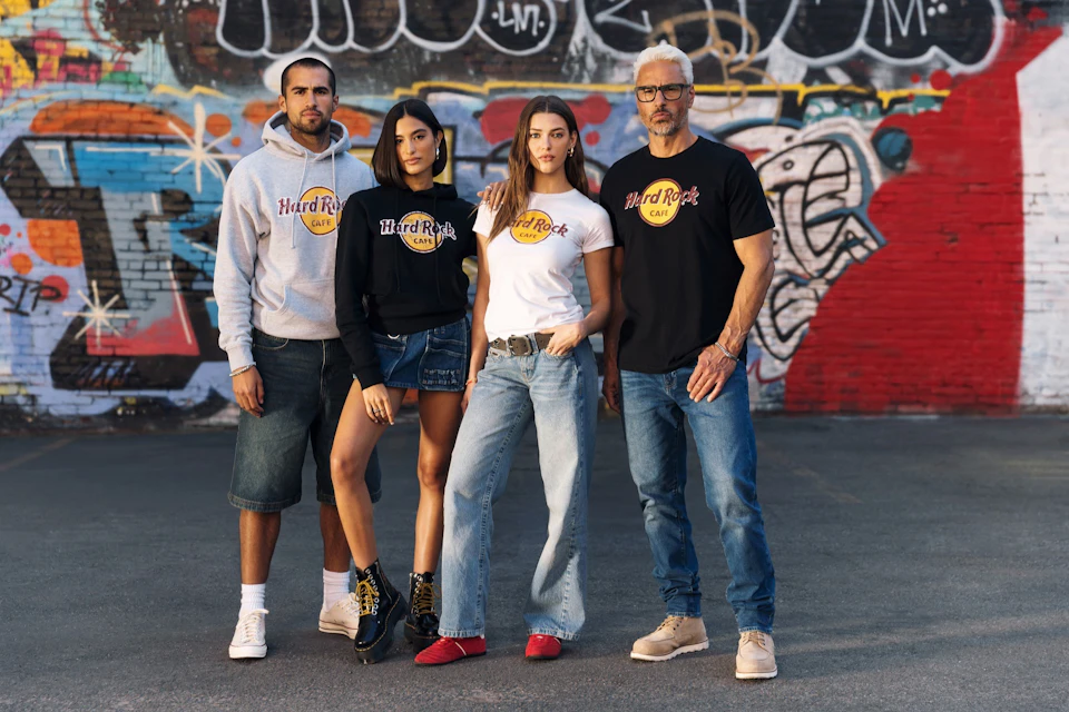 Four people wearing Hard Rock Cafe branded clothing stand in front of a colorful graffiti wall on a paved surface.