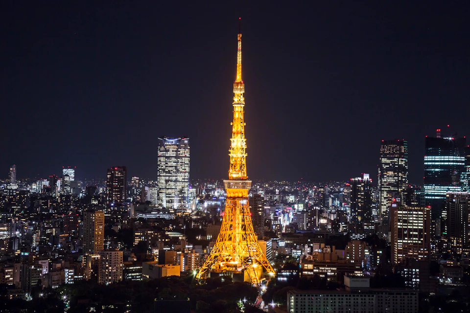 Illuminated Tokyo Tower at night, surrounded by city buildings and lights against a dark sky.