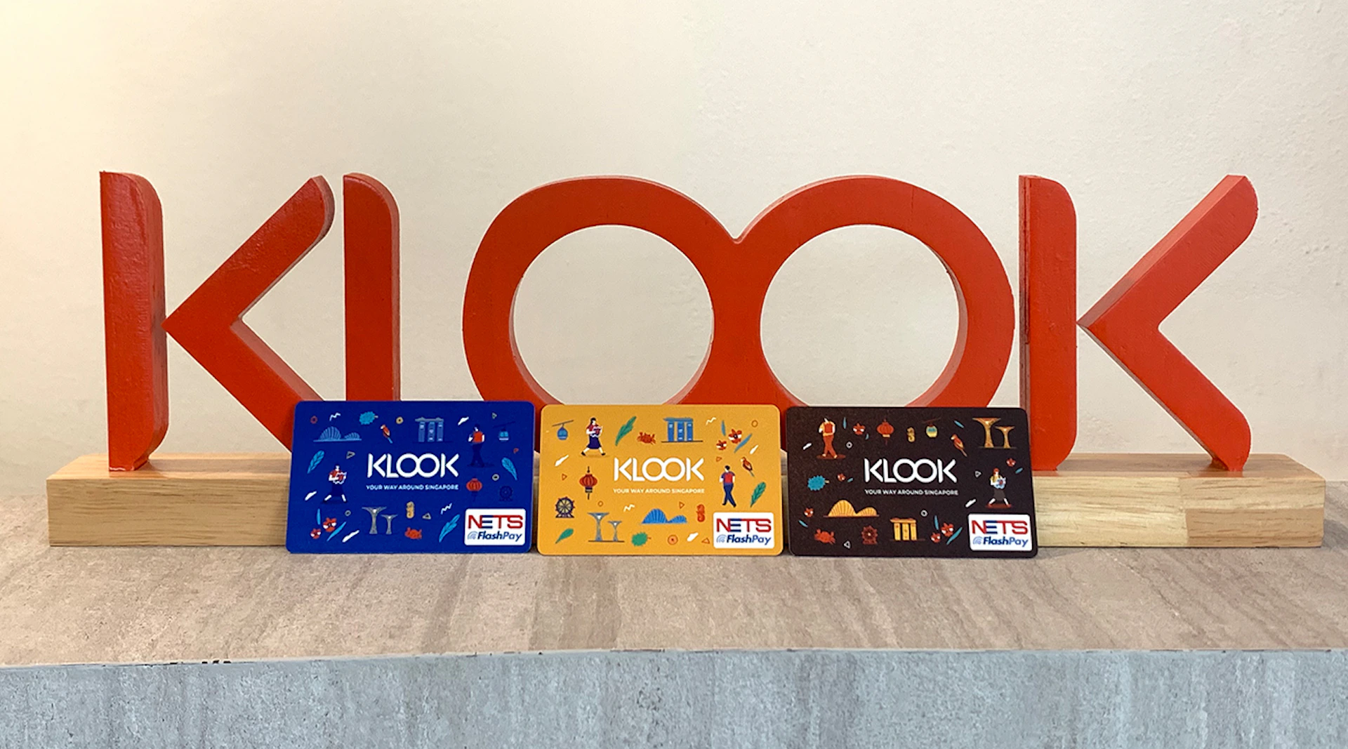 Three colorful Klook NETS FlashPay cards displayed in front of a large red "100" sign.
