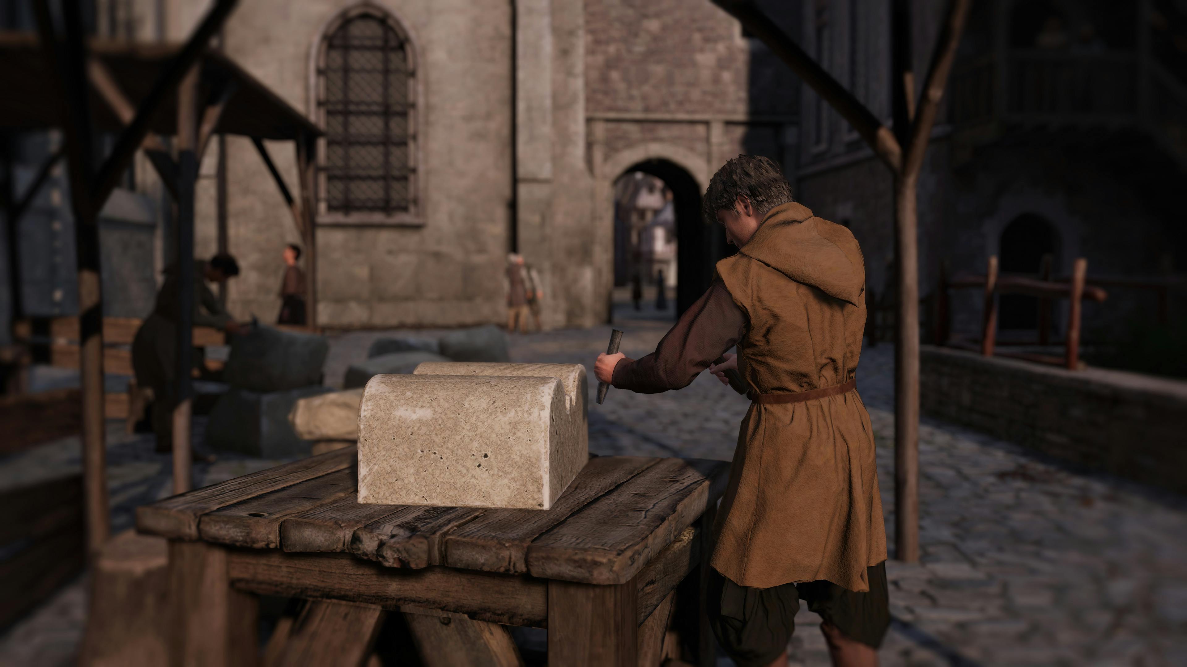 석조 건물을 배경으로 중세 복장을 한 사람이 자갈길의 나무 테이블에 돌 블록을 깍아 놓습니다.