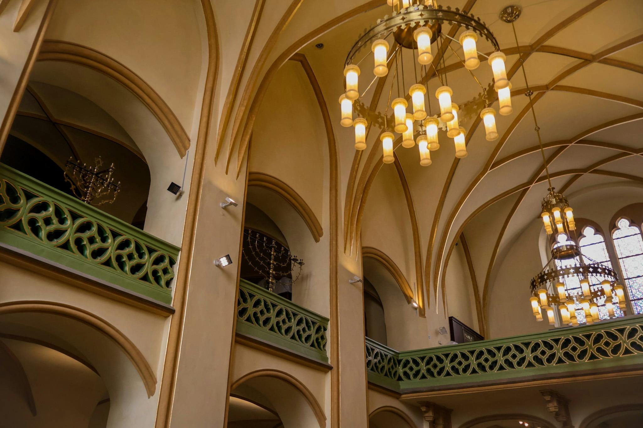 Interior of a building with arched ceilings, ornate chandeliers, and a decorative green railing on the upper level.