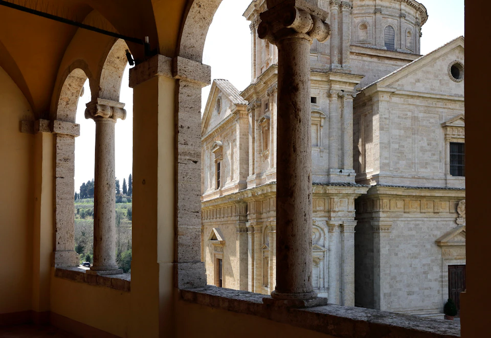 View of a historic stone building through a series of arches, with columns in the foreground and a landscape visible in the distance.
