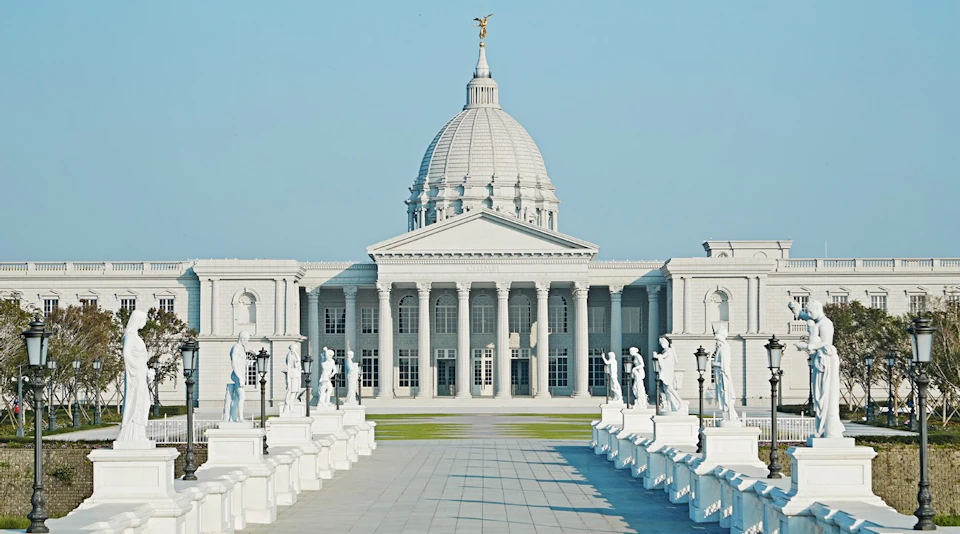 A neoclassical building with a large dome, columns, and statues along a pathway under a clear blue sky.