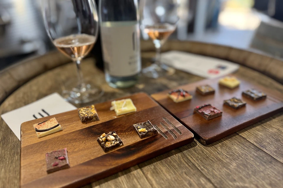 Small dessert squares arranged on wooden boards, accompanied by two glasses of rosé and a bottle on a wooden table.