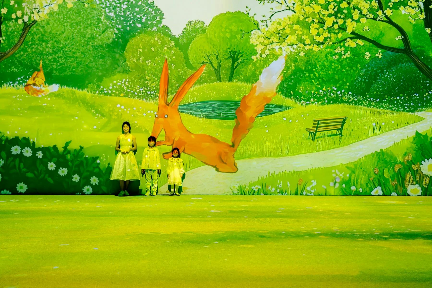 Tre persone in giallo si trovano davanti a un murale vivace e animato con un grande coniglio che salta e una scena di parco serena.