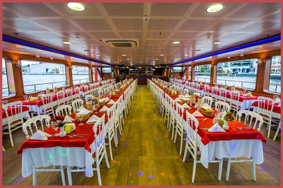 A large, elegantly set dining area on a boat with red and white table settings, arranged in long rows with windows on both sides.