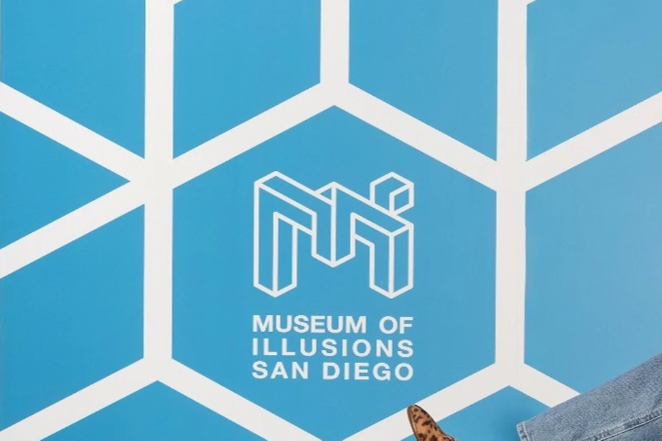 Two people in a room at the Museum of Illusions, appearing to vary in size due to the room's design and perspective.