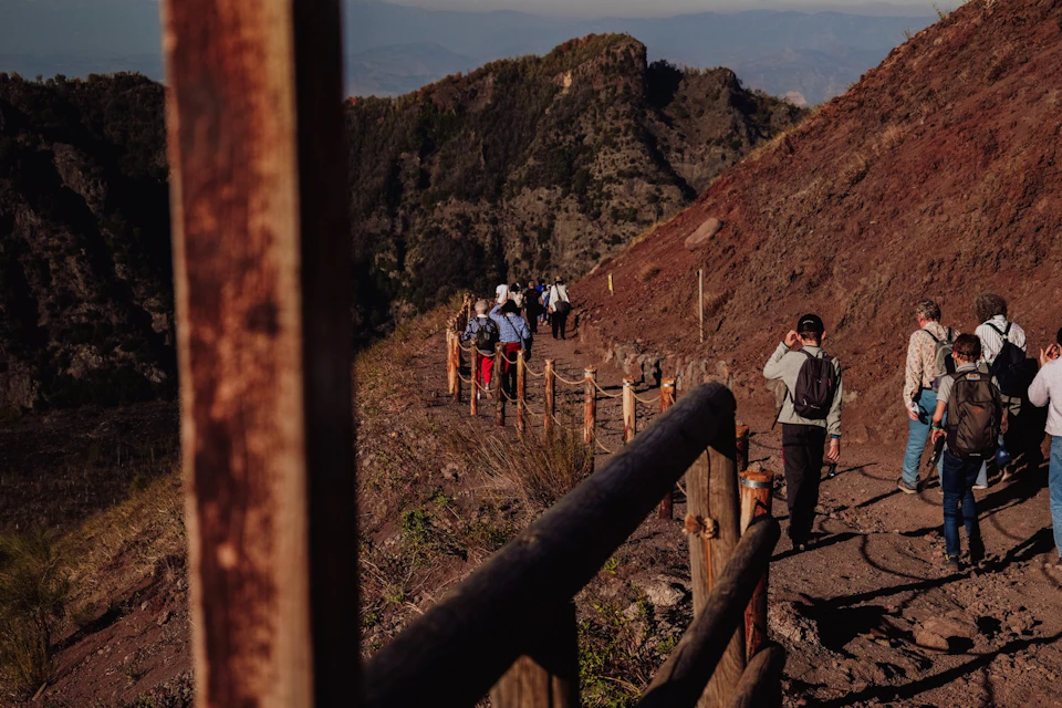 A group of people hiking along a fenced trail on a mountainside under clear skies.