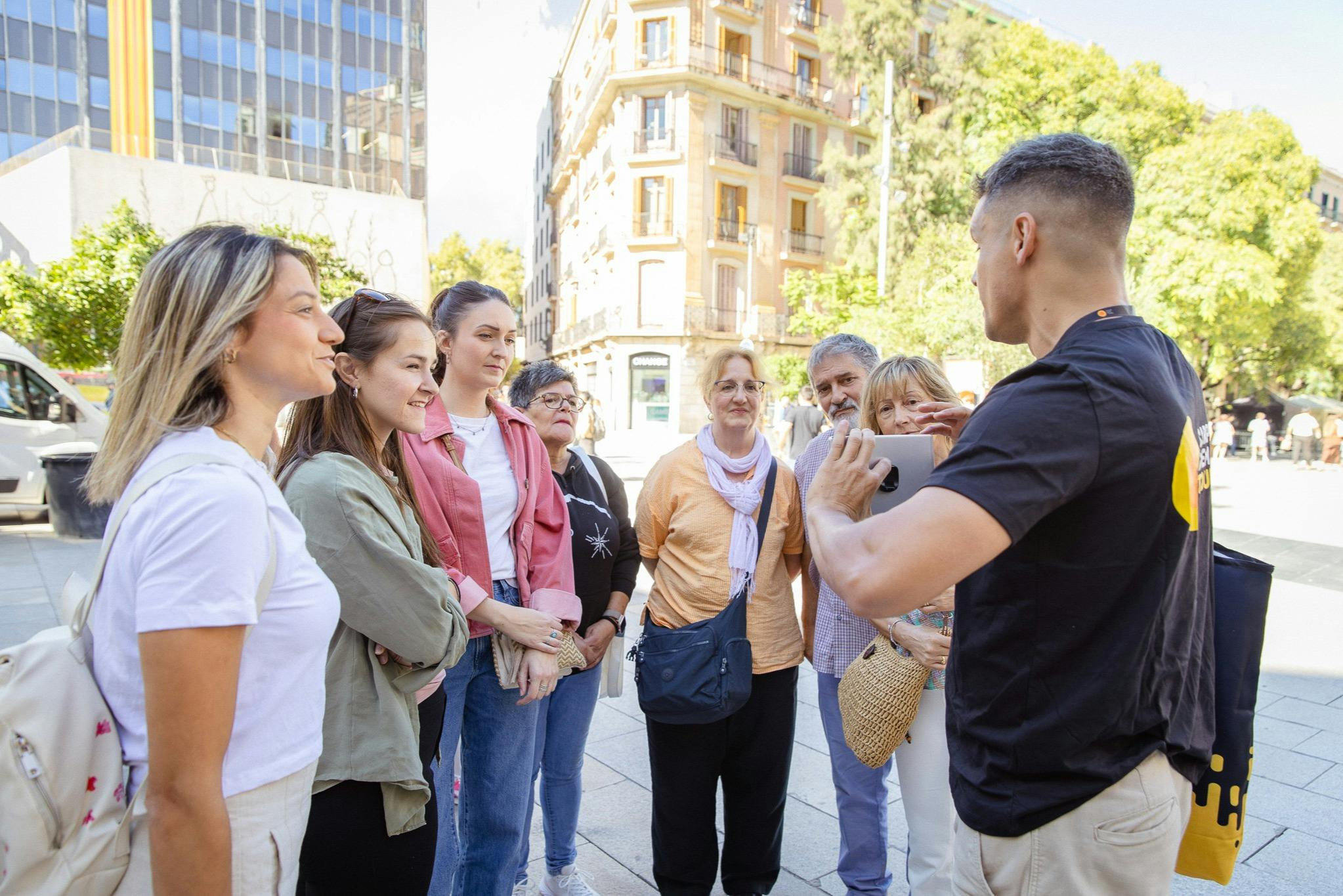 Un groupe de personnes se tenant à l'extérieur dans un environnement urbain, écoutant un guide tenant un appareil.