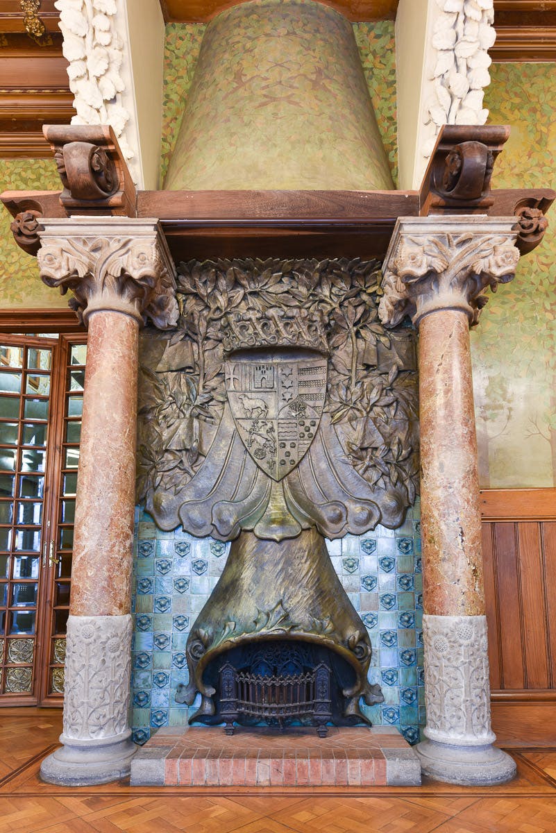 Cheminée ornée de colonnes de marbre, de sculptures complexes et d'un bouclier décoratif flanqué de feuilles. Foyer carrelé en dessous.