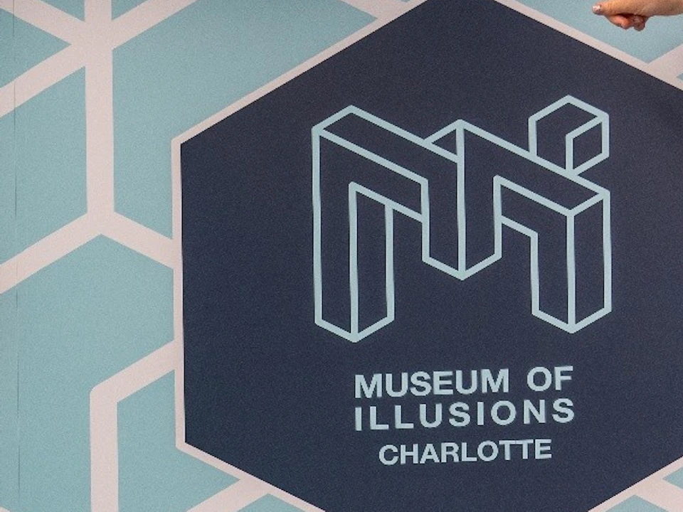 Two people in a room with geometric patterned walls at the Museum of Illusions in Charlotte, creating an optical illusion.