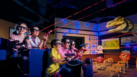A group of people wearing 3D glasses, aiming laser guns in an interactive dinosaur-themed game.