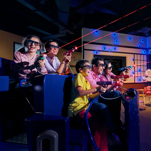 A group of people wearing 3D glasses, aiming laser guns in an interactive dinosaur-themed game.