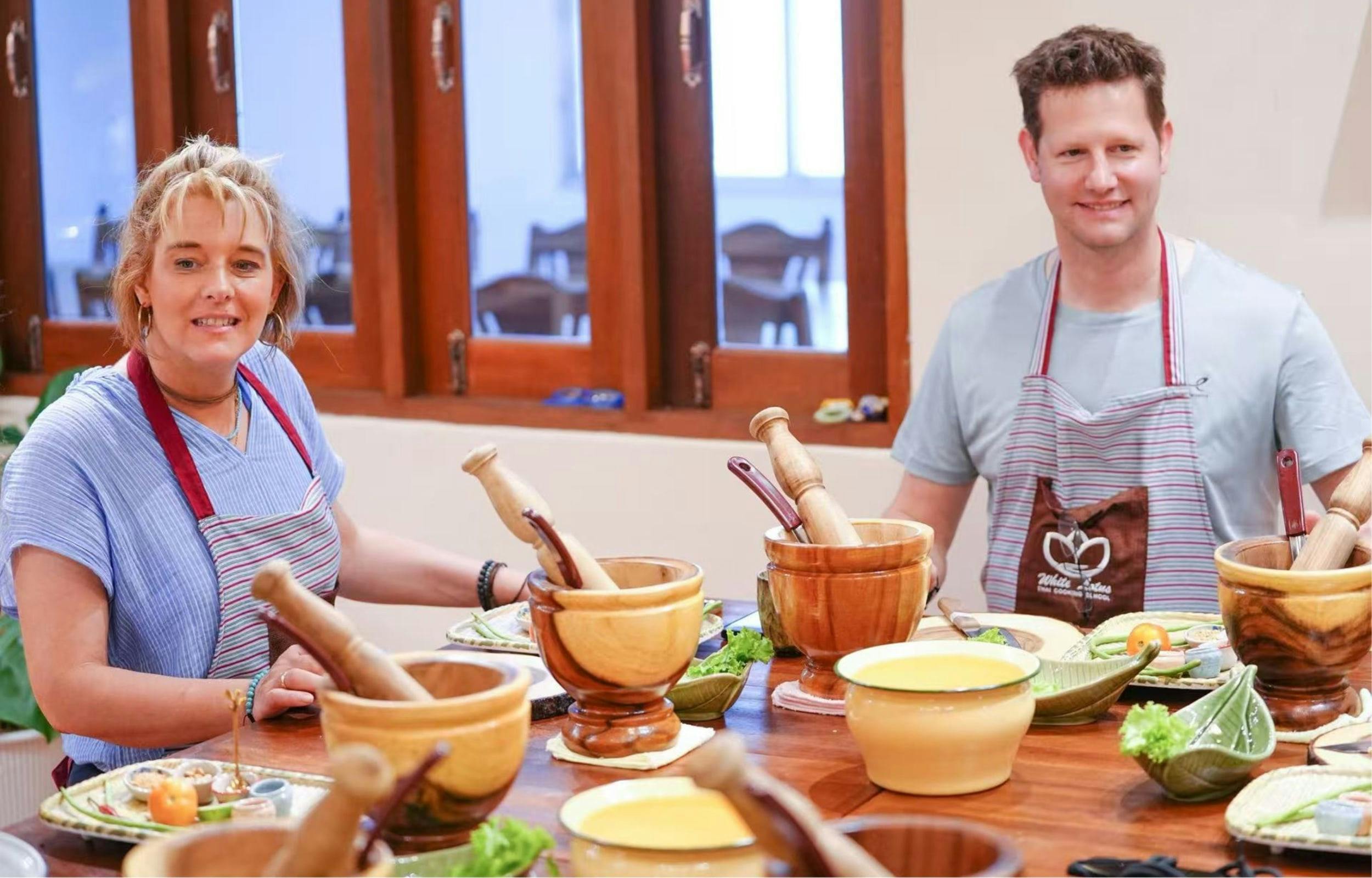 A person wearing an apron stands by a table set with wooden mortars, pestles, and bowls filled with ingredients.
