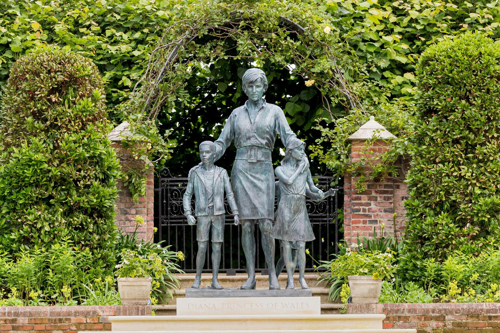 Statue of a woman with two children under an archway surrounded by greenery. "DIANA PRINCESS OF WALES" inscribed on the base.