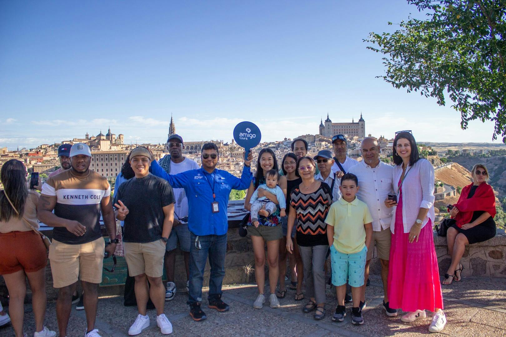 Μια ομάδα ανθρώπων που ποζάρουν για μια φωτογραφία σε εξωτερικούς χώρους με γραφική θέα σε ιστορικά κτίρια και ένα δέντρο στο παρασκήνιο.
