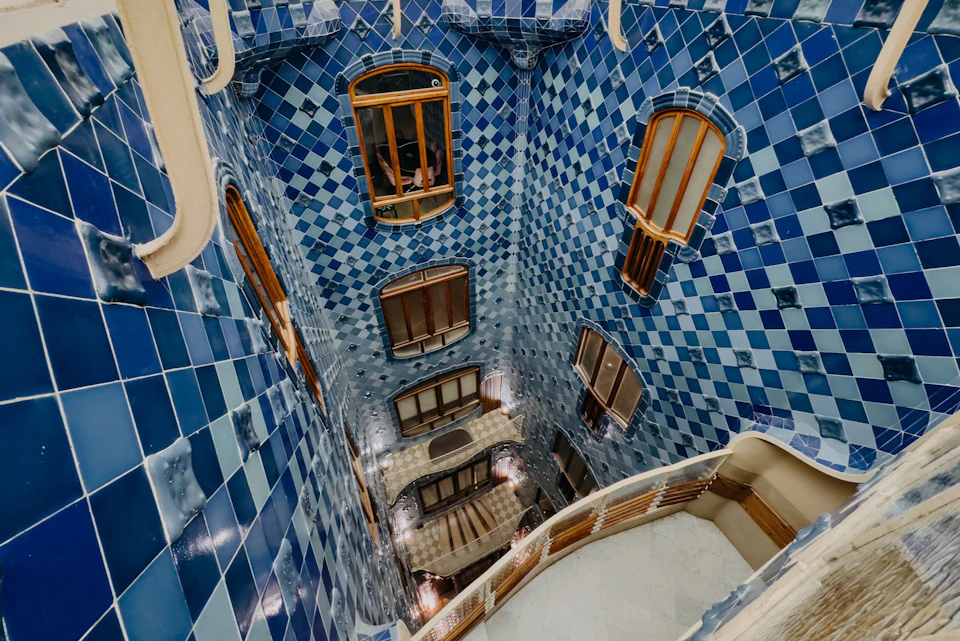 An interior vertical view of a blue tiled building with wooden window frames and an ornate, curved railing staircase.