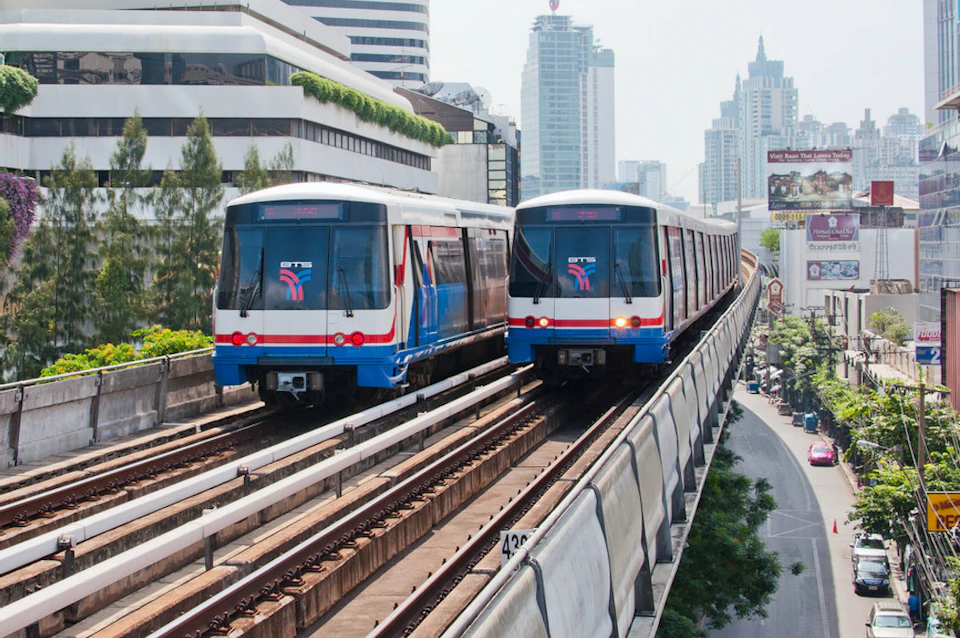 Two metro trains on elevated tracks in an urban area with modern buildings in the background on a clear day.
