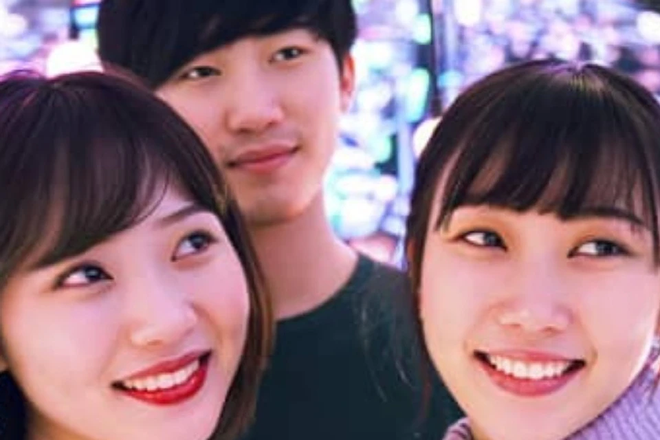 Three people smiling and posing for a selfie in front of a colorful, illuminated background with light orbs.