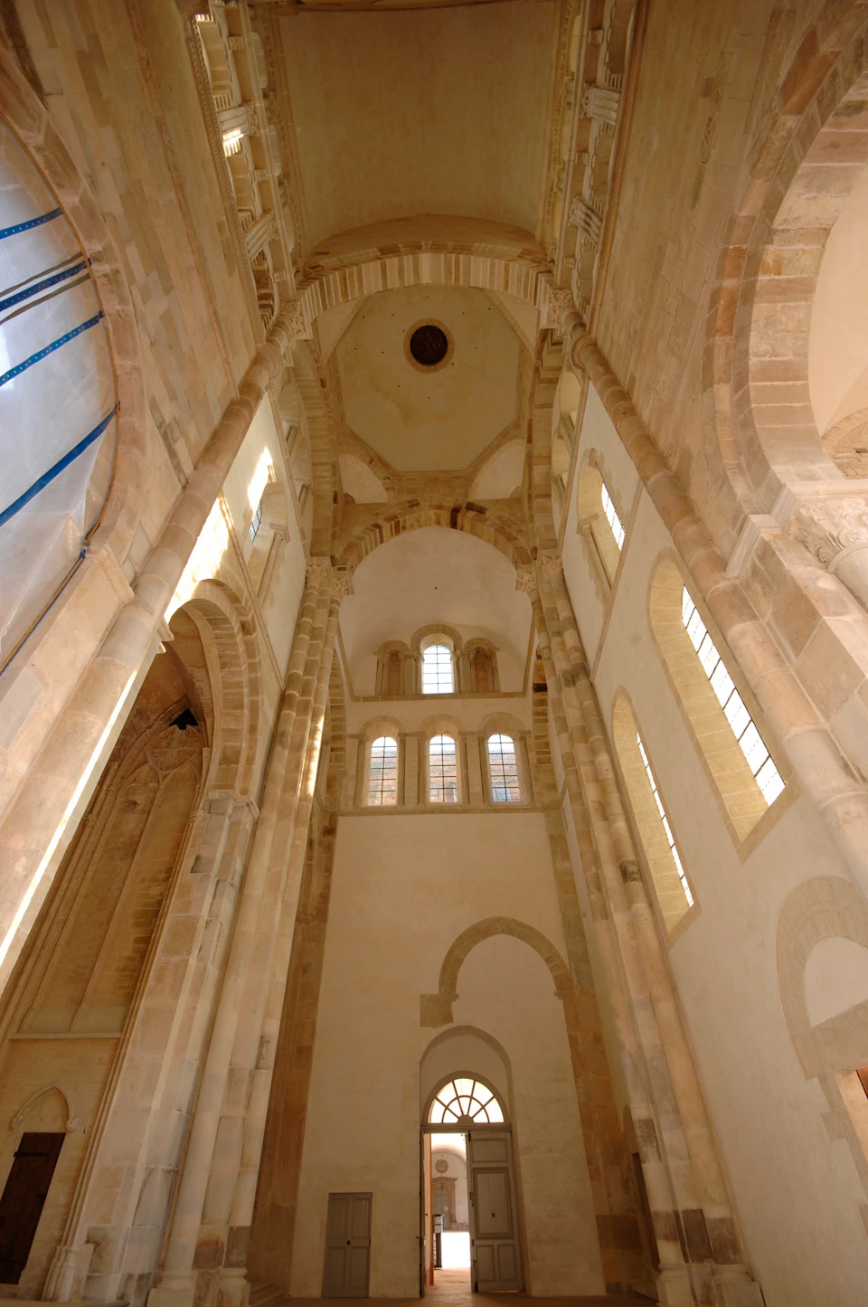 Interior of a tall, historic building with arched windows and stone columns, viewed from the ground looking up.