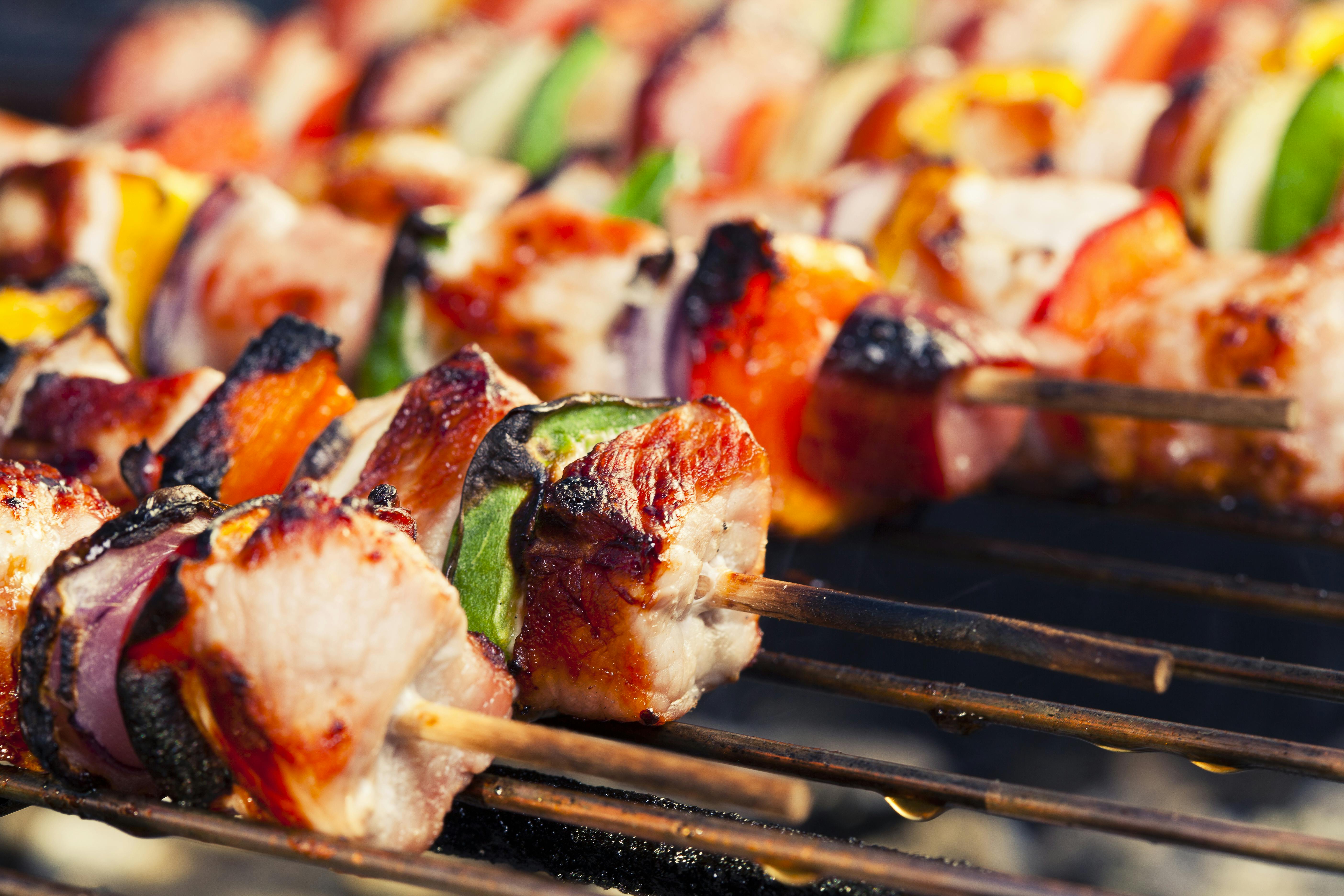 Close-up of grilled meat and vegetable skewers on a barbecue grill, featuring charred meat, peppers, and zucchini.