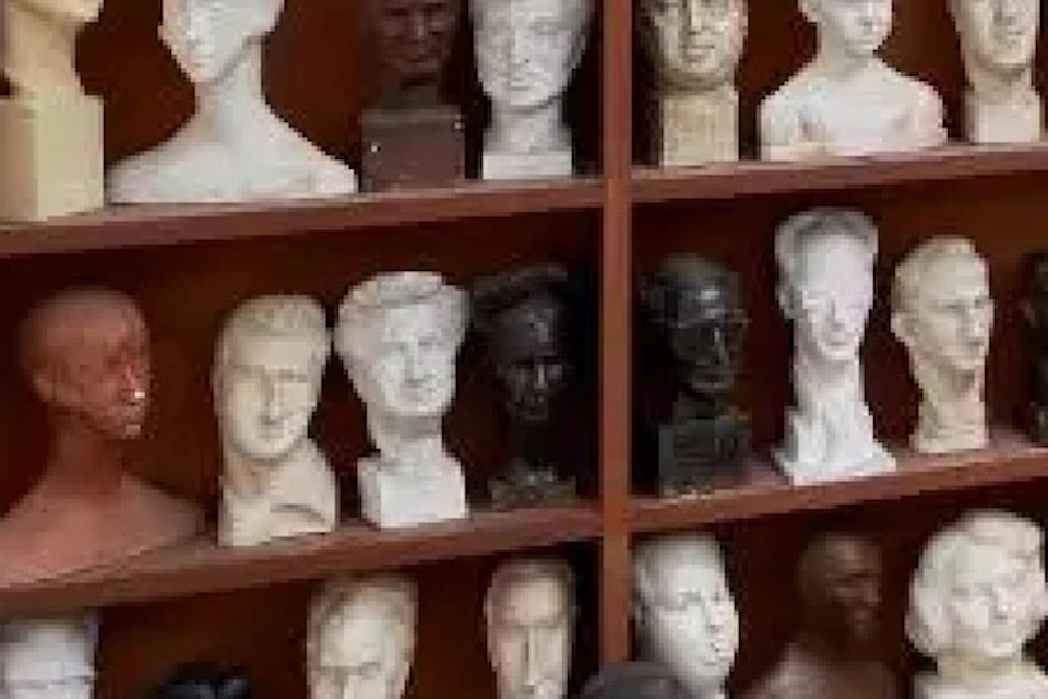A gallery room displaying numerous bust sculptures on shelves and various statues placed on pedestals.