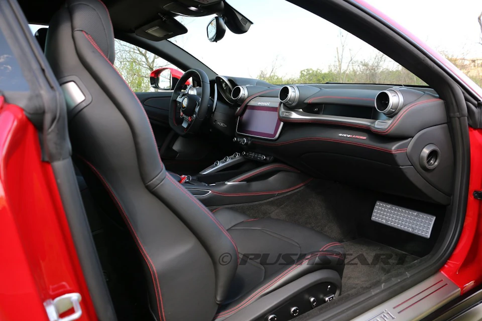 Interior of a modern sports car with black seats, red stitching, a touchscreen dashboard, and a steering wheel with controls.
