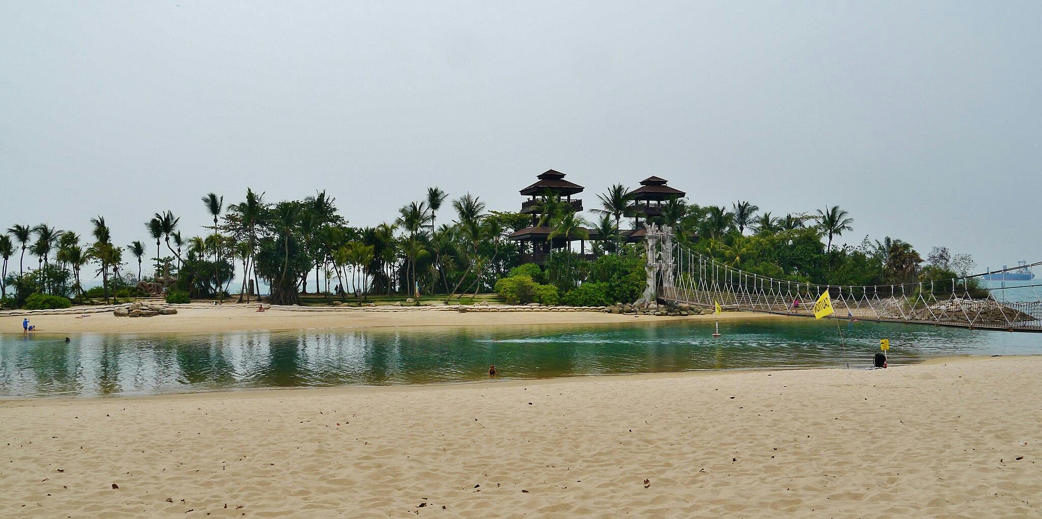 热带沙滩，有棕榈树、绳索吊桥和几个人，靠近平静的水体。