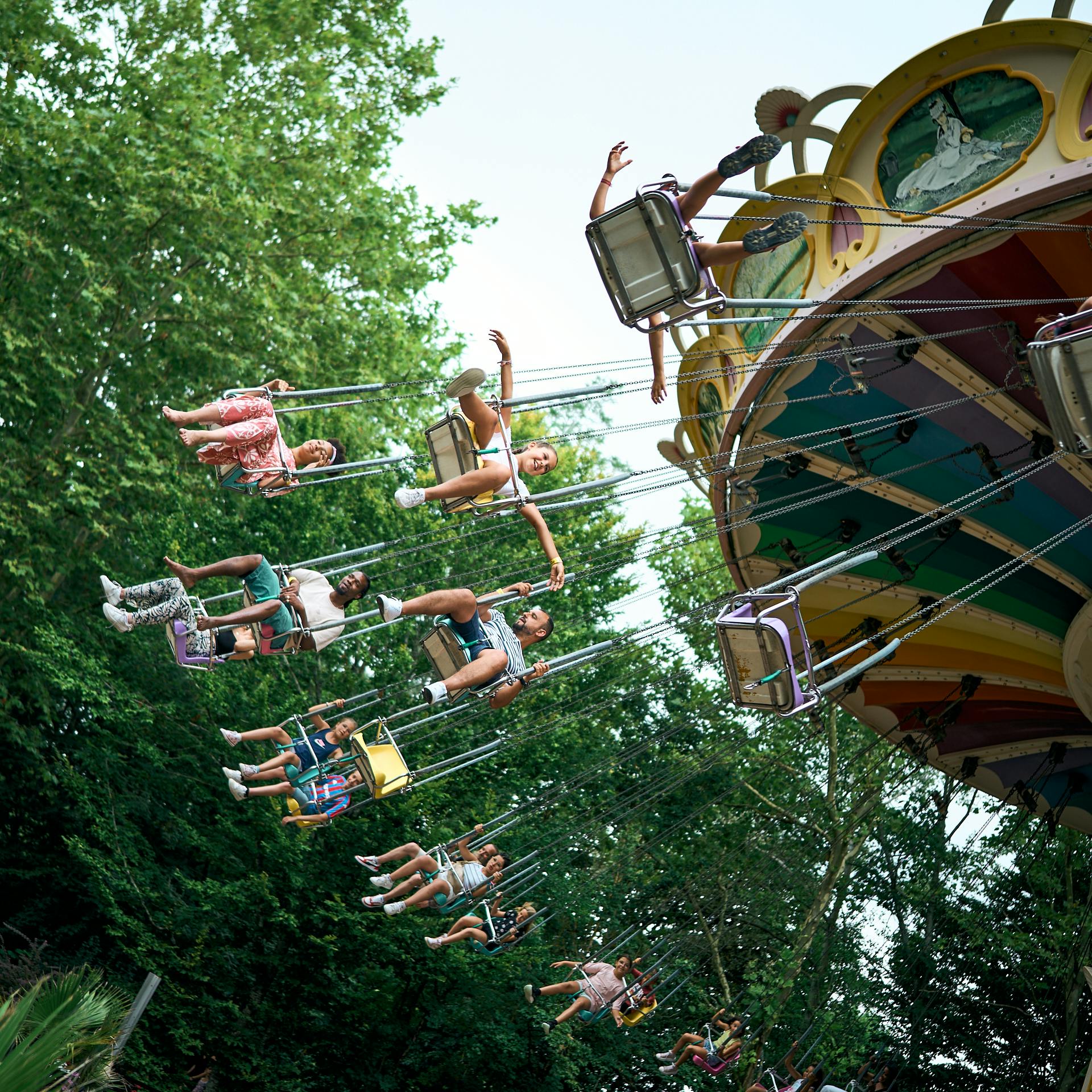 Lidé si užívají pestrou jízdu na houpačce na veletrhu se svěžími zelenými stromy v pozadí.